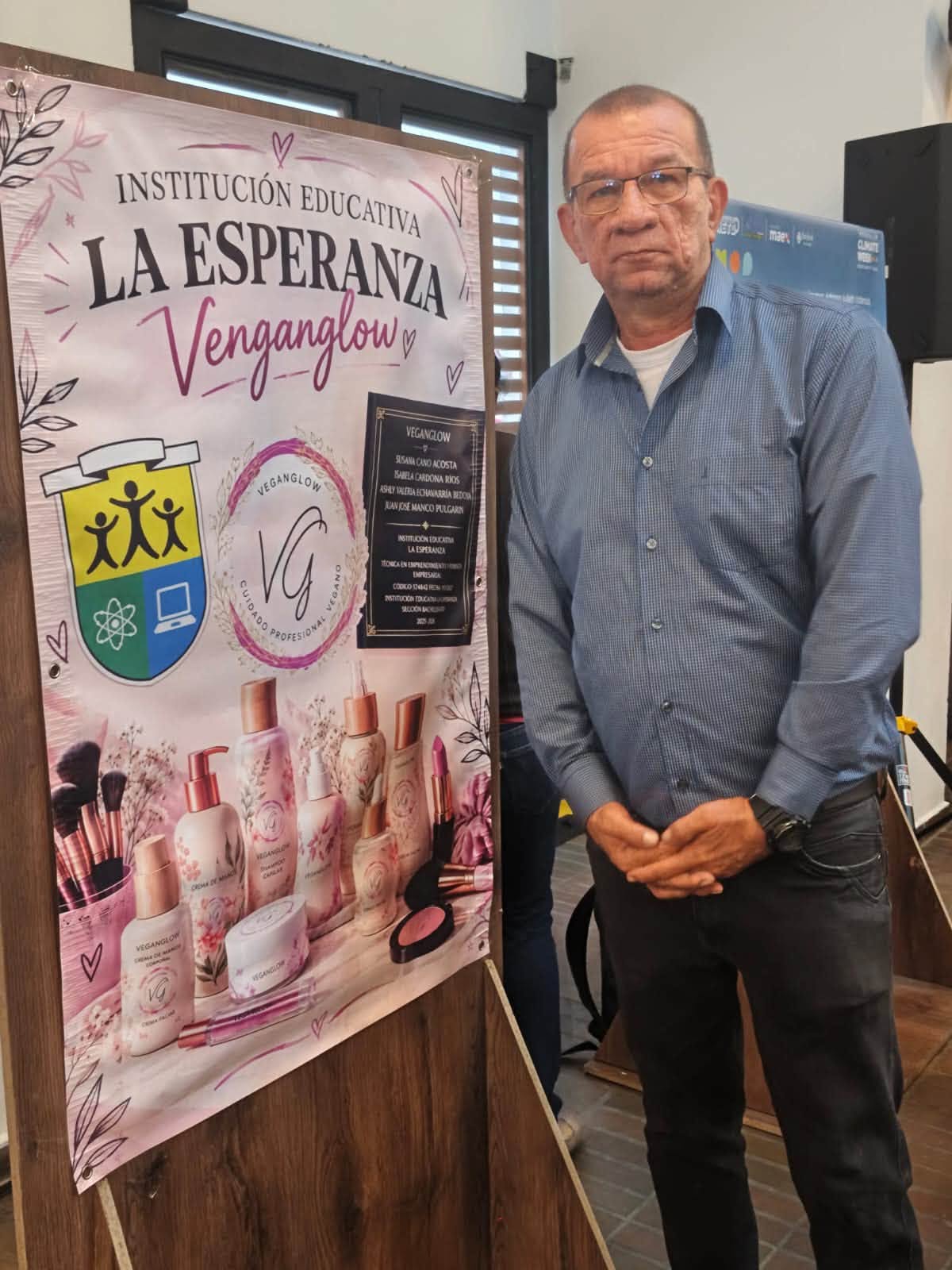 El docente José posa al lado de un cartel con publicidad del proyecto